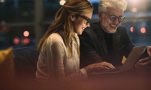 A man and woman seated on a couch, focused on a laptop screen together.