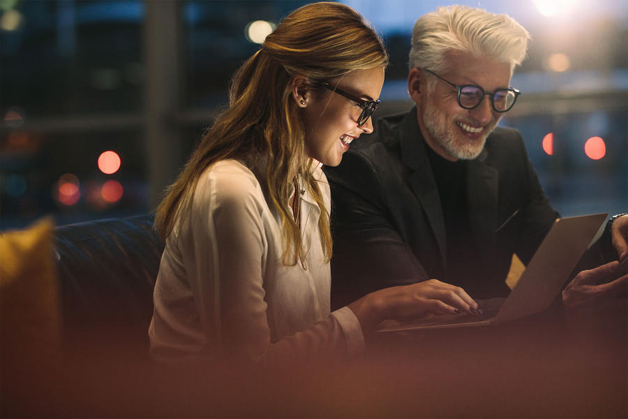 A man and woman seated on a couch, focused on a laptop screen together.