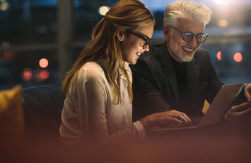 A man and woman seated on a couch, focused on a laptop screen together.
